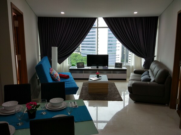 Una sala moderna con un sofá azul, un sofá gris, una mesa de centro y un televisor sobre un mueble.