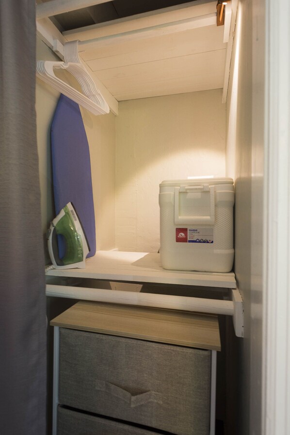 A compact storage area with a white ironing board, a blue ironing board cover, a white plastic container, and a green iron.