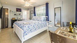 A bedroom with a bed, a desk with a chair, a ceiling fan, a window with curtains, and a door.