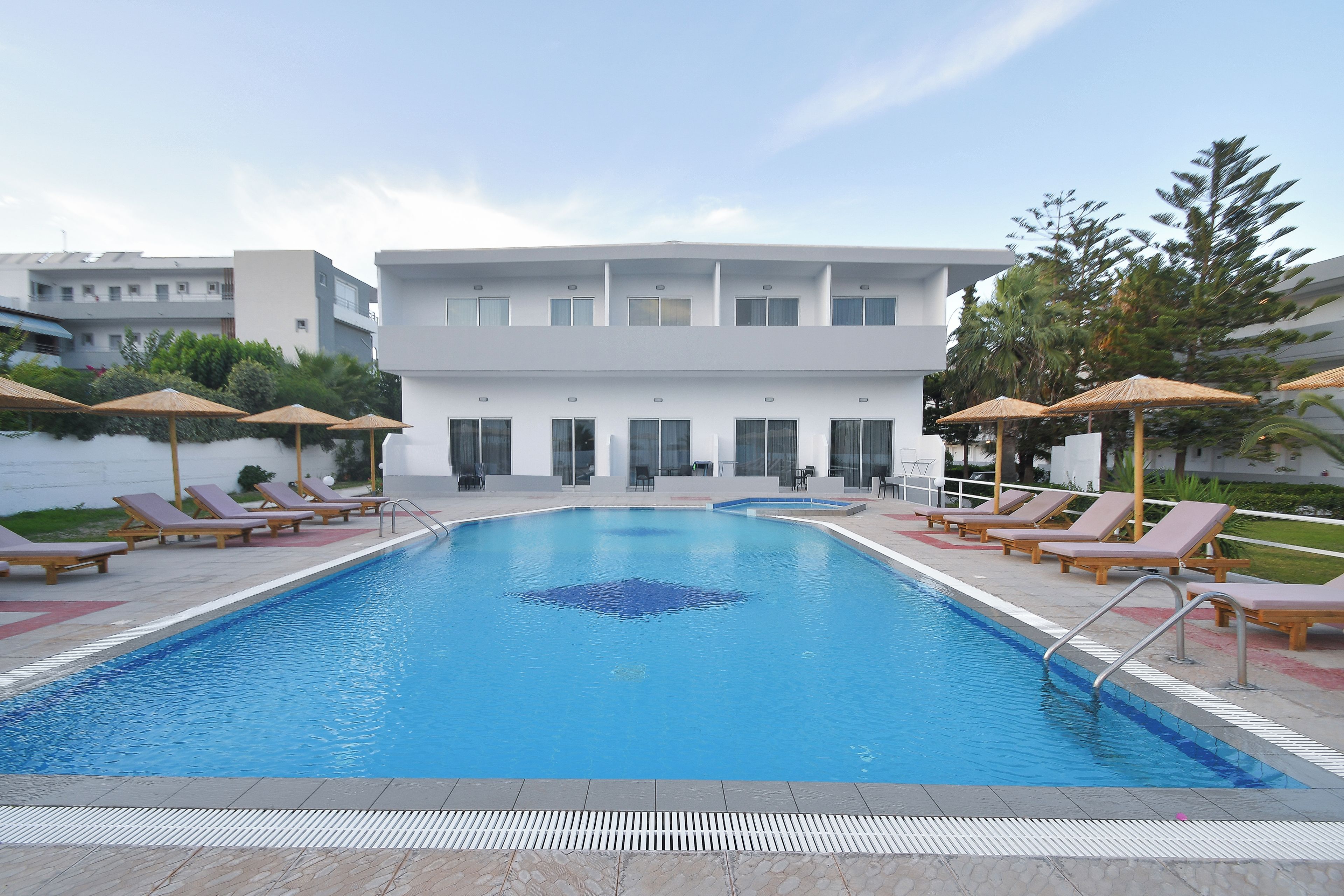 Piscina com espreguiçadeiras e guarda-sóis, cercada por um edifício moderno com amplas janelas.