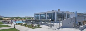 A modern building with large windows, a pool, and outdoor seating. - Evita Bay (Rhodes)