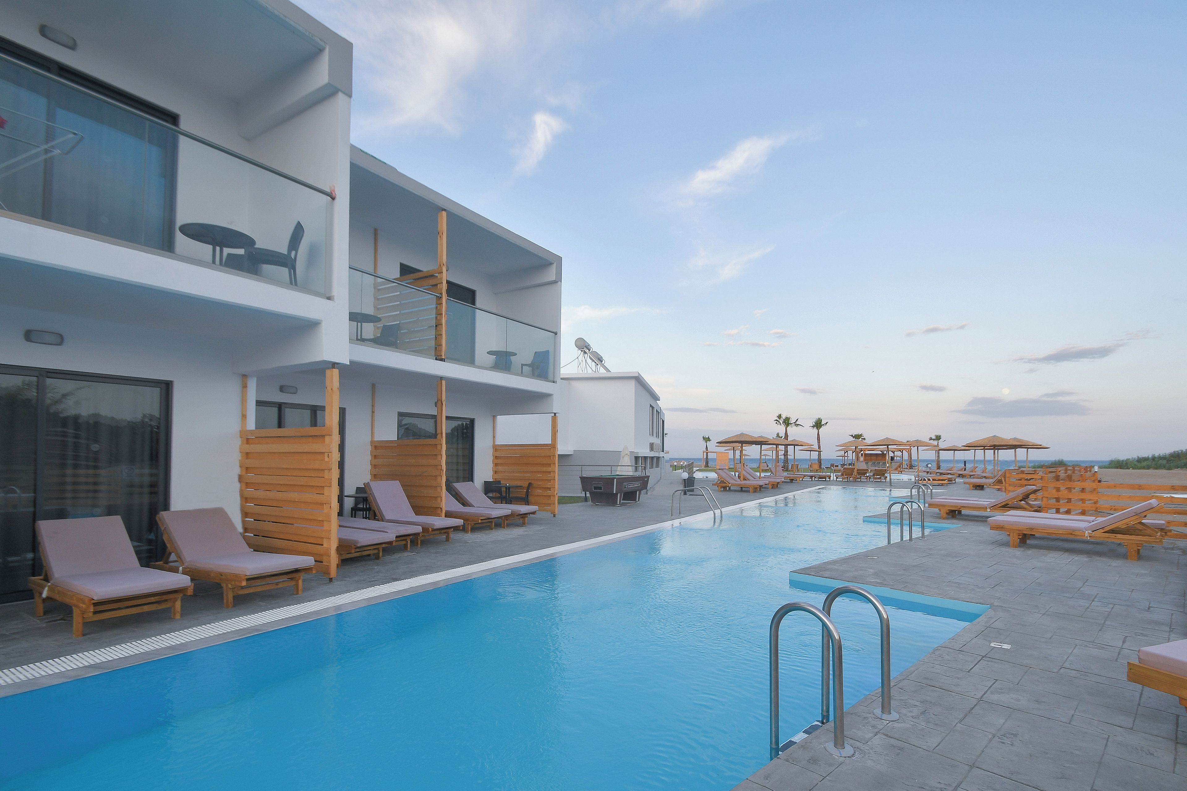 Un hotel moderno con piscina en la azotea, tumbonas y cielo despejado.