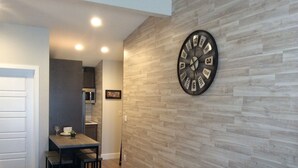 A modern room with a wooden wall clock, a bed, a dining table with chairs, and a kitchen area in the background. - Chic Denver Tech studio (Centennial)