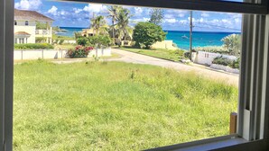 Vista desde una habitación con ventana que da a un área verde, una carretera y una escena costera con edificios y el océano.