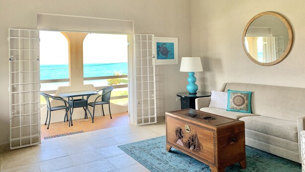 Una habitación con vista al océano, un cofre de madera, un sofá, una mesa con sillas y una lámpara.