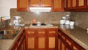A kitchen with wooden cabinets, granite countertops, a stove, and a sink. - Downtown Cabo San Lucas Suite with Ocean and Harbor Views (Cabo)