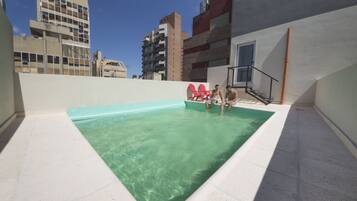 A rooftop swimming pool with clear water, surrounded by buildings.