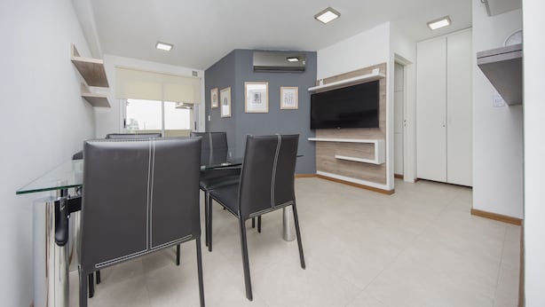 Une cuisine moderne avec un coin repas, comprenant une table en verre, des chaises noires et des étagères intégrées.