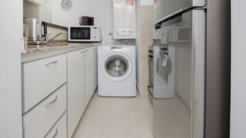 A compact kitchen with a washing machine, microwave, and a small refrigerator.