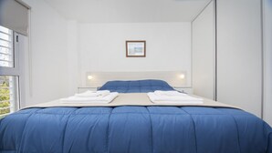 A neatly made bed with a blue duvet, white pillows, and folded towels on a white headboard. - WX4 Venezuela Apartment (Córdoba)