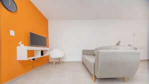 A modern living room with a grey sofa, a white chair, and a flat-screen TV mounted on an orange wall. - WX4 Venezuela Apartment (Córdoba)