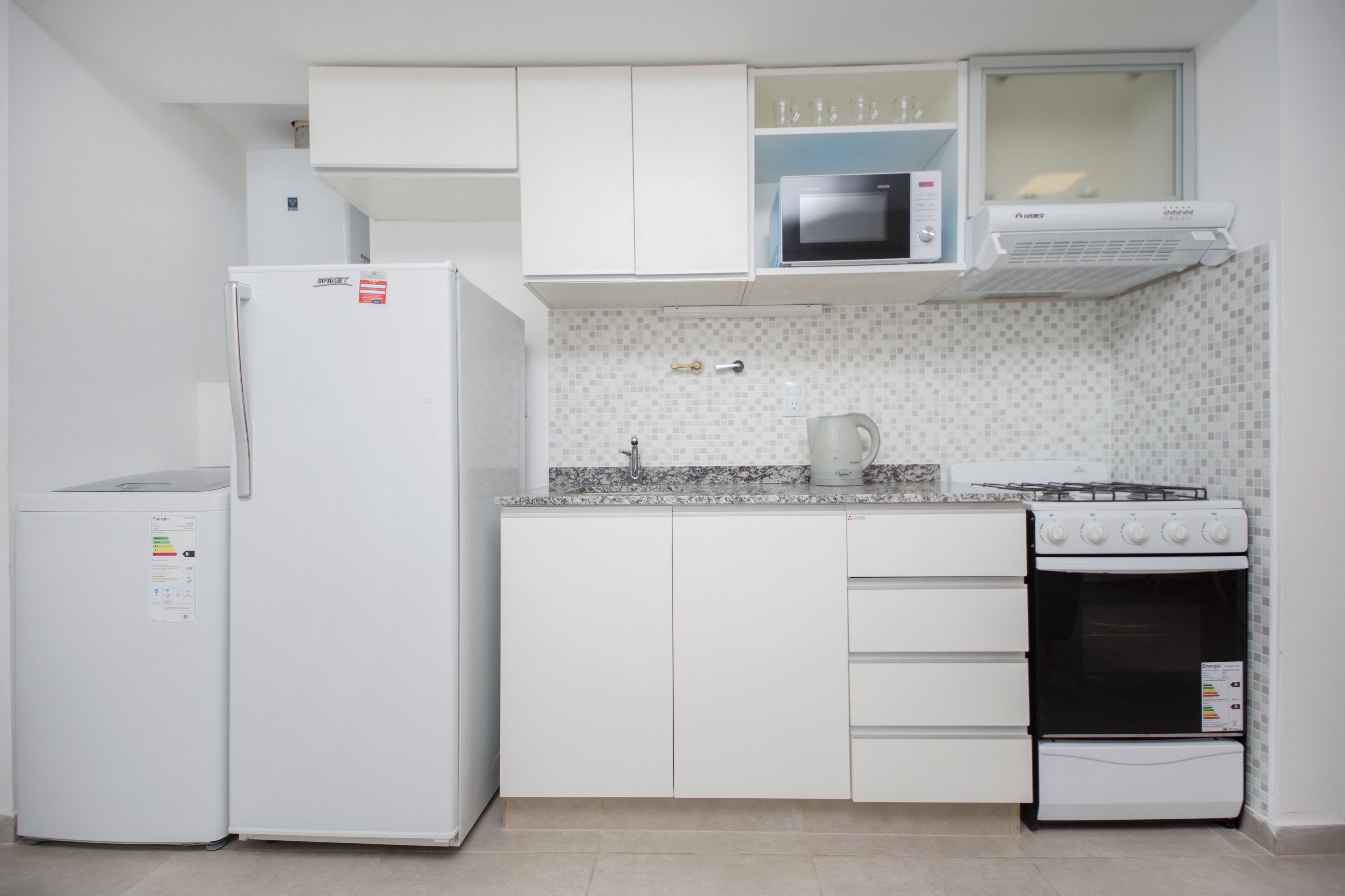 A compact kitchen with white cabinetry, a microwave, a stove, and a refrigerator.