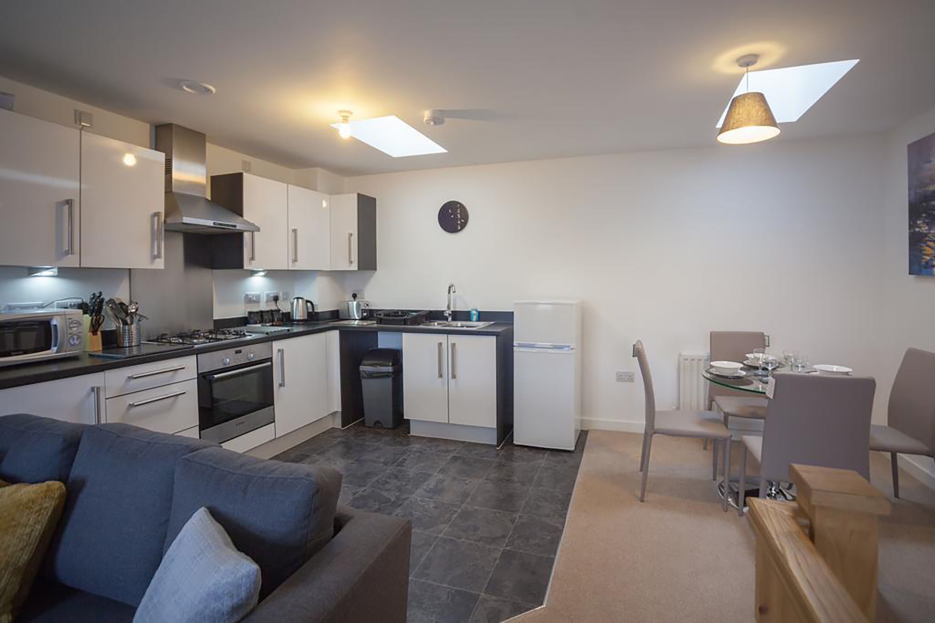 A modern kitchen with white cabinets, a dining area with a table and chairs, and a gray sofa.