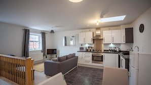 A modern kitchen with white cabinets, a dining area with a glass table, and a living room with a sofa and a TV. - The Robin Coach House (Hereford)