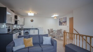A modern apartment with a grey sofa, a dining area, and a kitchen. - The Robin Coach House (Hereford)
