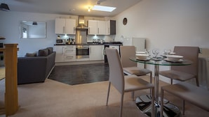 A modern kitchen with white cabinets, a microwave, and a dining area with a glass table and chairs. - The Robin Coach House (Hereford)