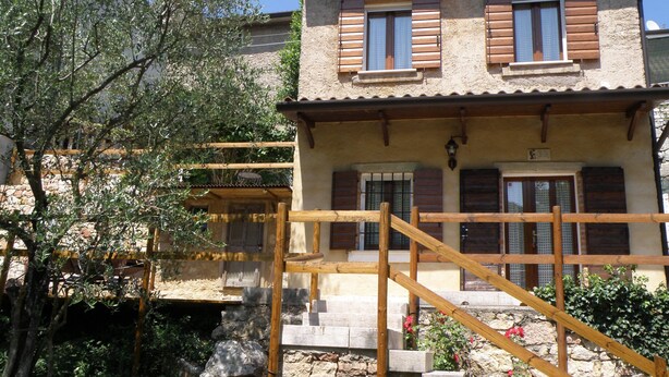 A rustic stone building with wooden shutters, a stone staircase, and a wooden pergola.