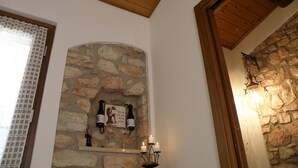 A stone fireplace with wine bottles and glasses, a wooden ceiling, and a stone wall.