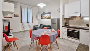 A compact living space with a dining area, kitchenette, and a sofa in the background.