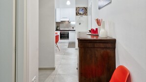 A hallway with a wooden cabinet, a red chair, and a dining table.
