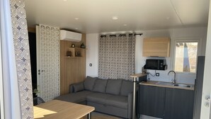 Um espaço de estar compacto com sofá, pequena mesa de jantar, cozinha compacta e cortina estampada.