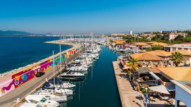 Uma marina com barcos atracados ao longo de uma orla, apresentando murais coloridos e uma vista clara do mar.