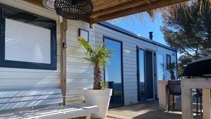 Um deck de madeira com um banco branco, uma palmeira em vaso e um edifício moderno com grandes janelas e uma porta.