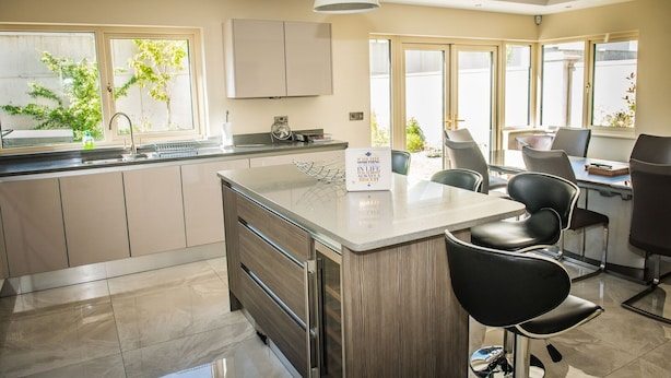 Een moderne keuken met een centraal eiland, een eethoek met stoelen en grote ramen.