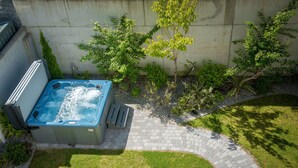 Een hottub in een achtertuin met een pad van bakstenen en begroeiing.