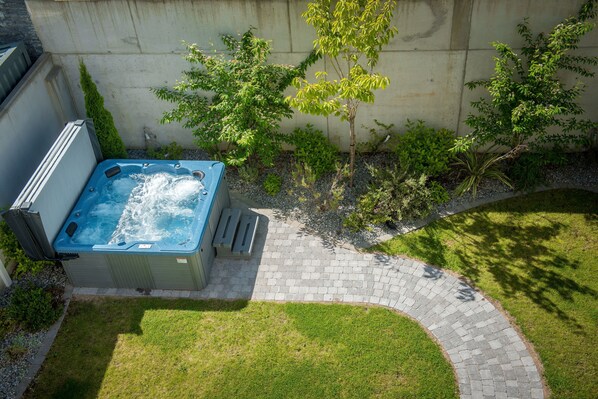 Un jacuzzi installé dans un jardin, avec un chemin en briques et de la verdure.