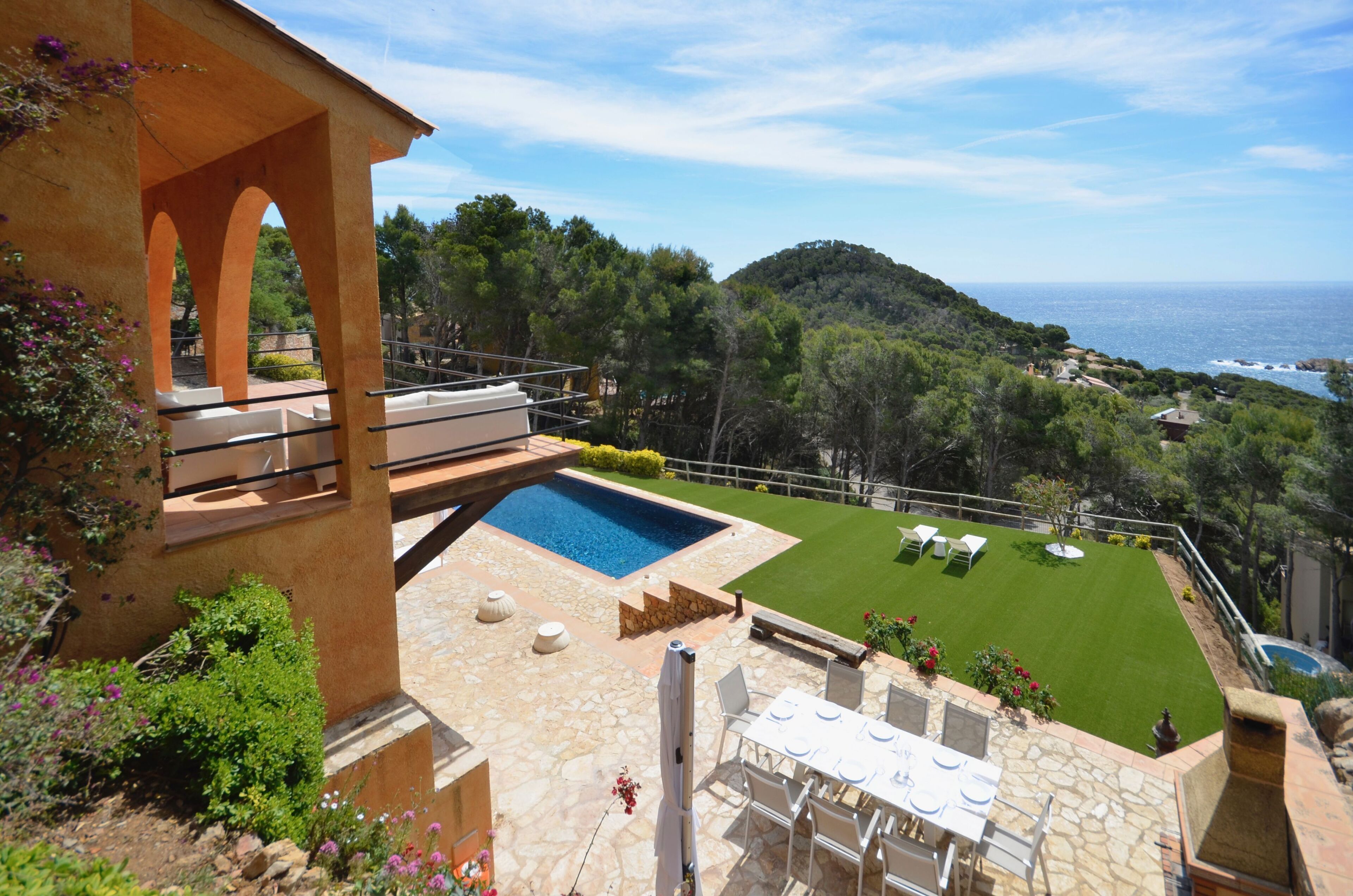 Un área de piscina con vista al mar, un césped bien cuidado y mobiliario exterior.