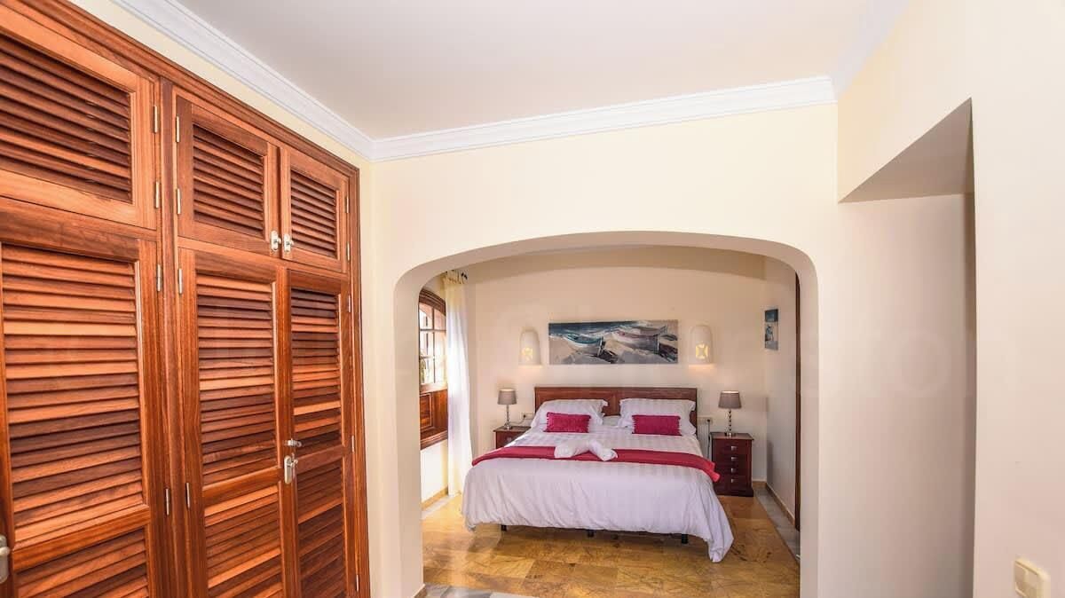 A bedroom with a bed, a wooden wardrobe, and an arched doorway.