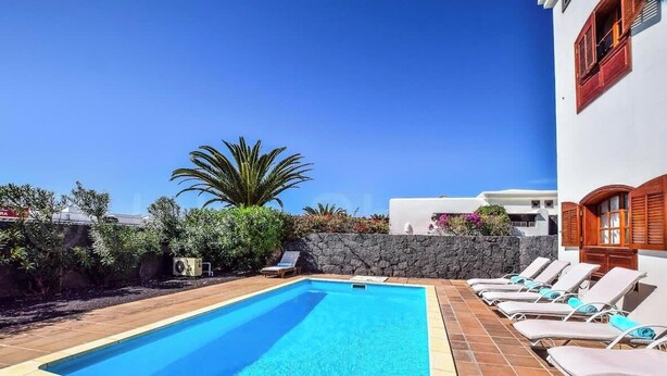 Una piscina con lettini, un muro in pietra e un cielo azzurro terso.