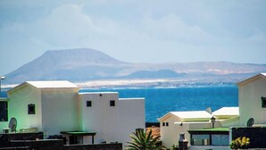 Paesaggio costiero con edifici bianchi, una montagna sullo sfondo e il mare in primo piano.