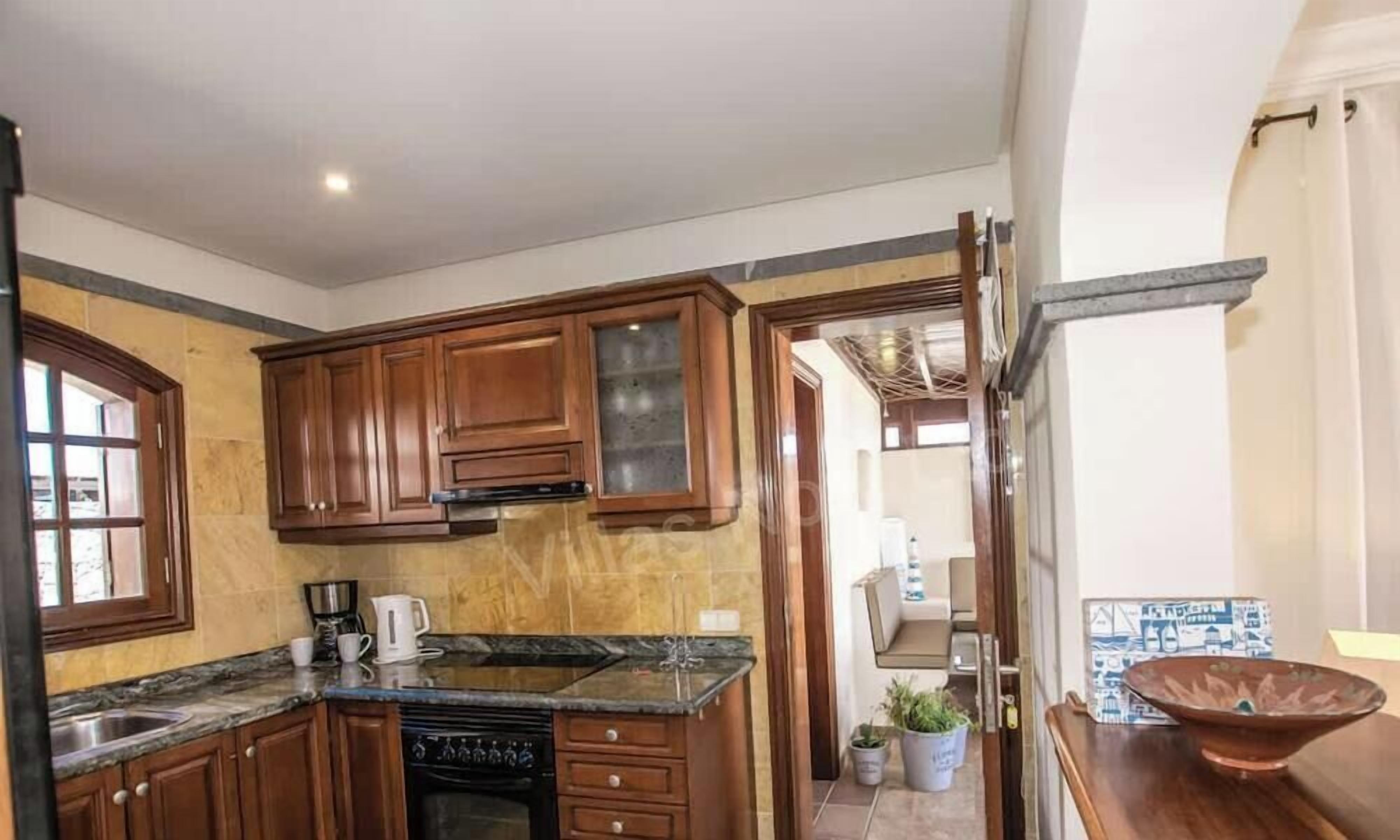 A compact kitchen with wooden cabinets, a built-in oven, and a coffee maker.