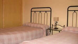 Habitación doble con dos camas, una mesita de noche con lámpara y una cortina.