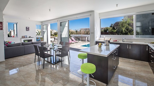 Une cuisine moderne dotée d’un grand îlot central, d’un coin repas avec des chaises et d’une vue sur une piscine.