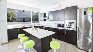 Une cuisine moderne avec des meubles de couleur sombre, un grand îlot central et un réfrigérateur en acier inoxydable.