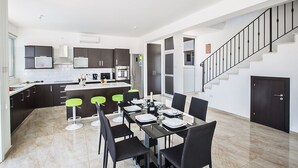 Une cuisine moderne avec des meubles de couleur sombre, un îlot central et un coin repas comprenant des chaises noires et une table dressée pour quatre personnes.