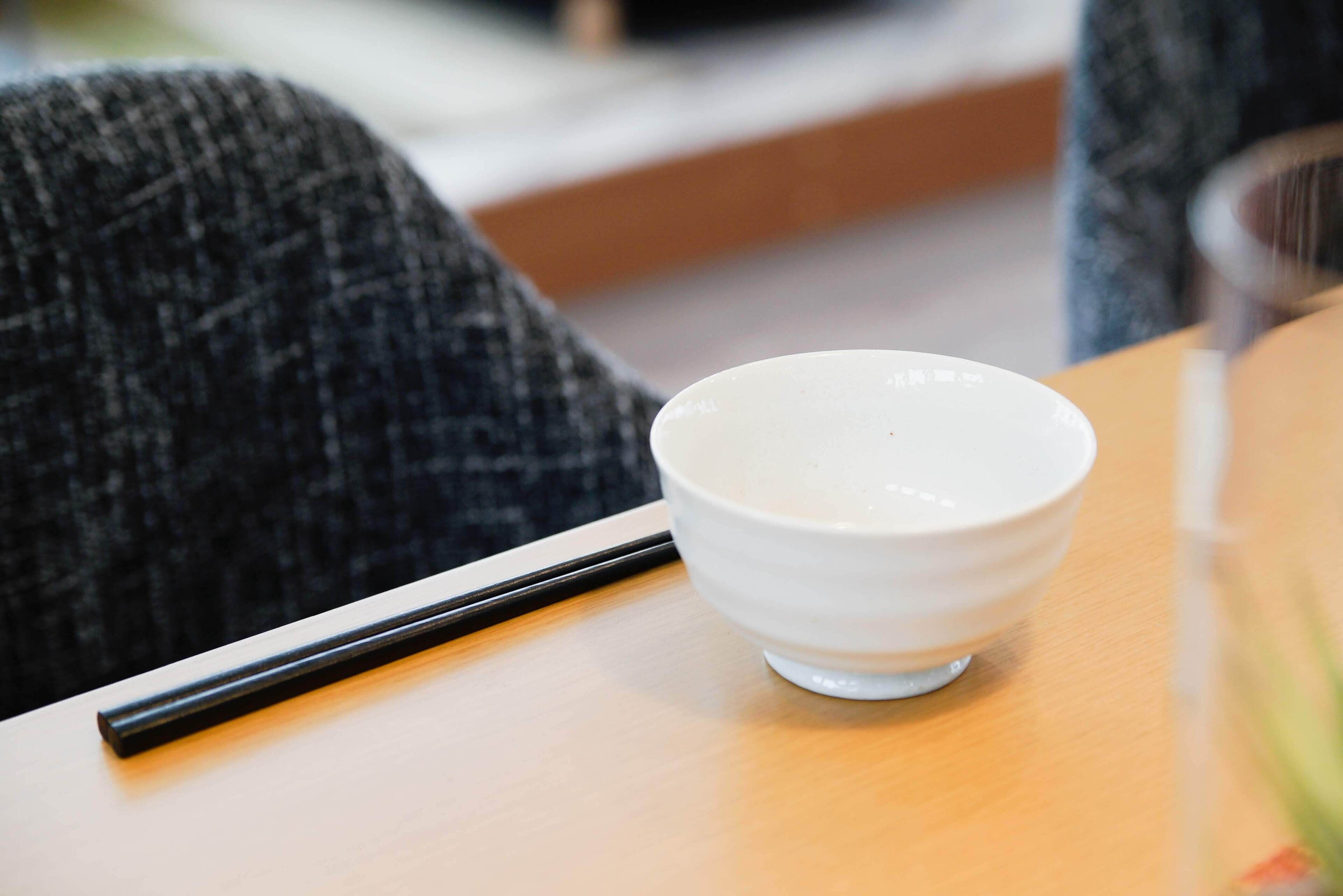 A white bowl on a wooden table with a black chopstick beside it.