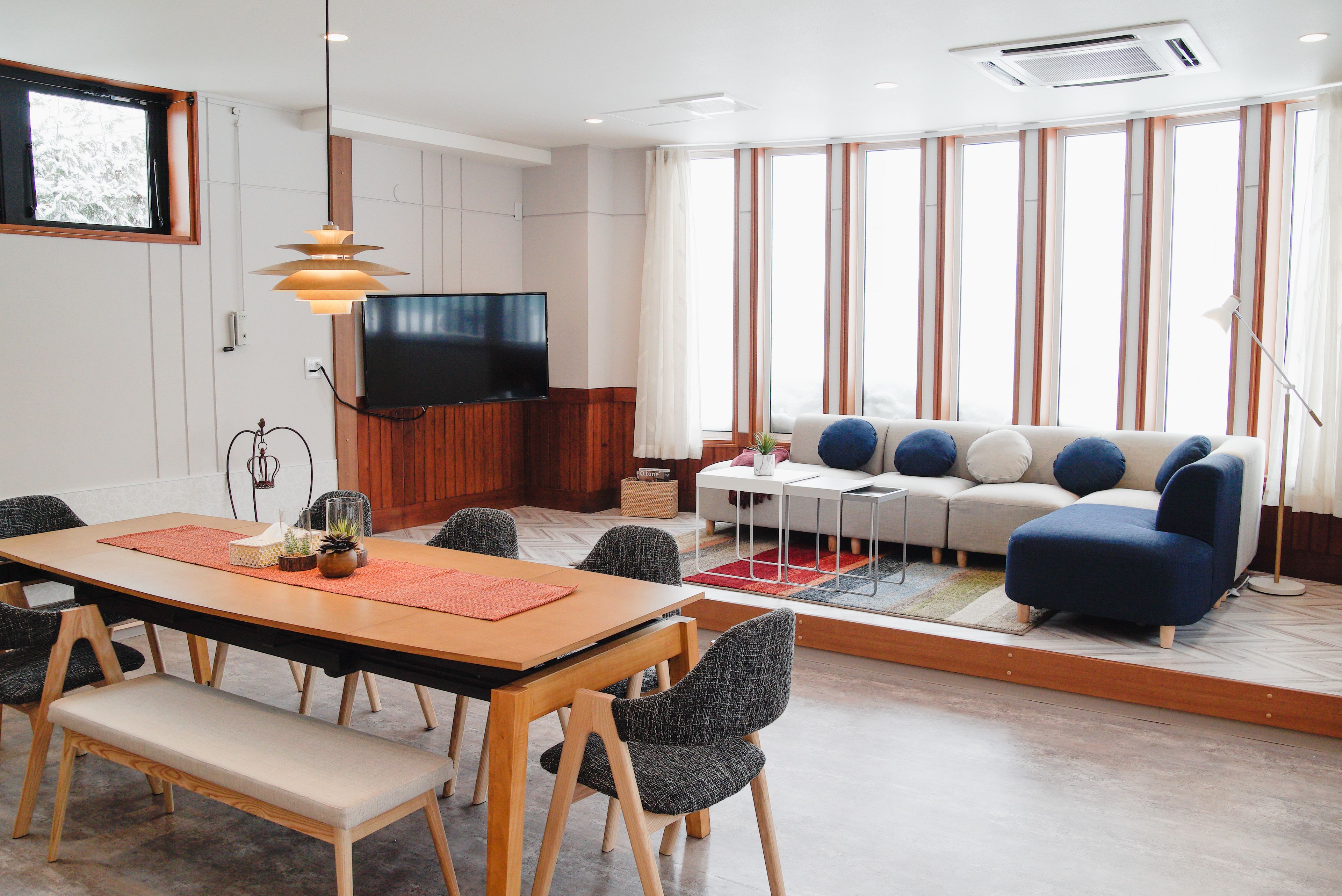 A modern living room with a dining area, a sofa set, and a TV mounted on the wall.