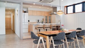 A modern kitchen with wooden cabinets, a central island, and a dining area with a wooden table and chairs. - Jstyle STAY Furano (Furano)