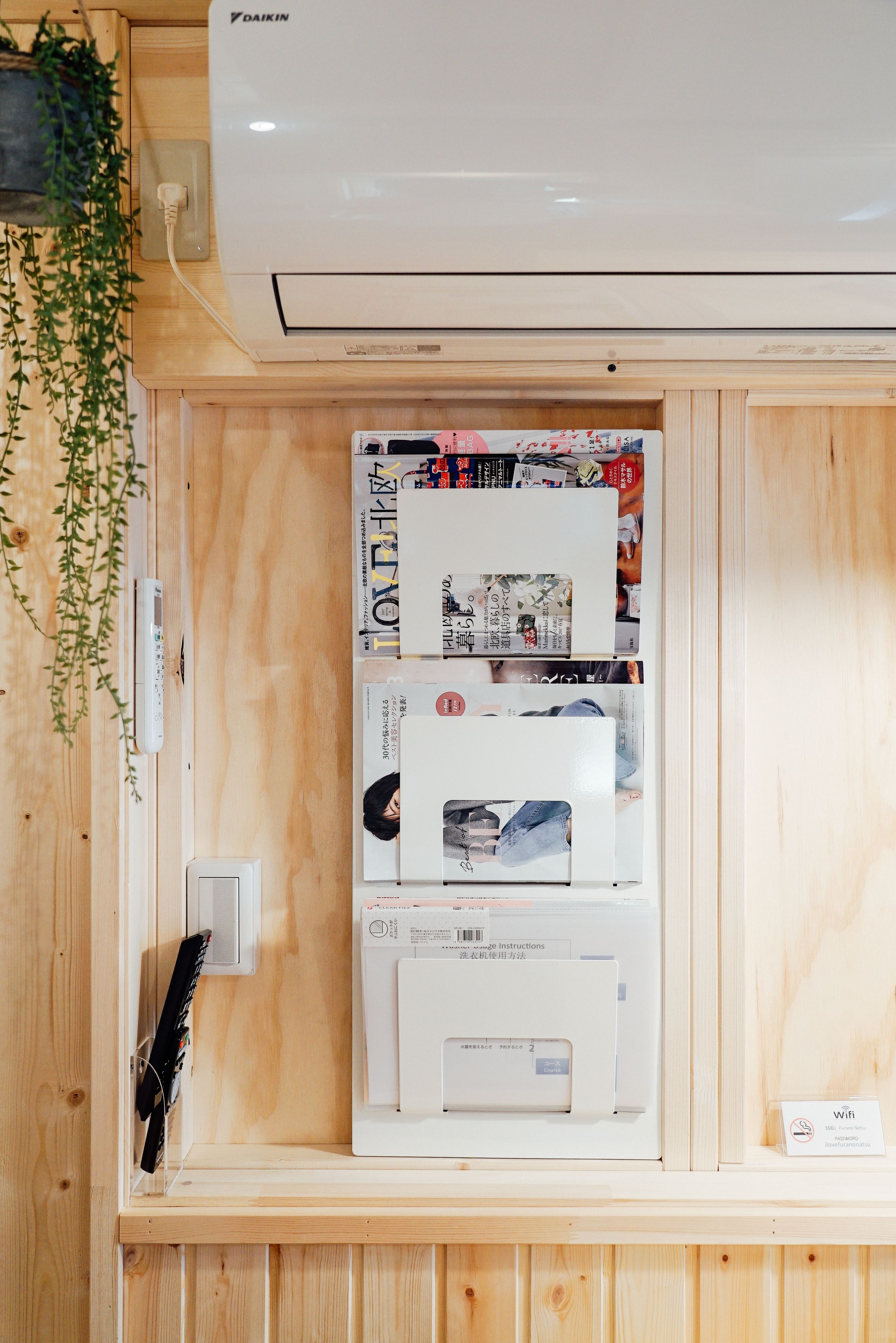 A wooden cabinet with a Daikin air conditioner mounted above it. Inside the cabinet, there are several items including a white device with a barcode, a white box with a picture of a person, and a small sign with a Wi-Fi symbol.