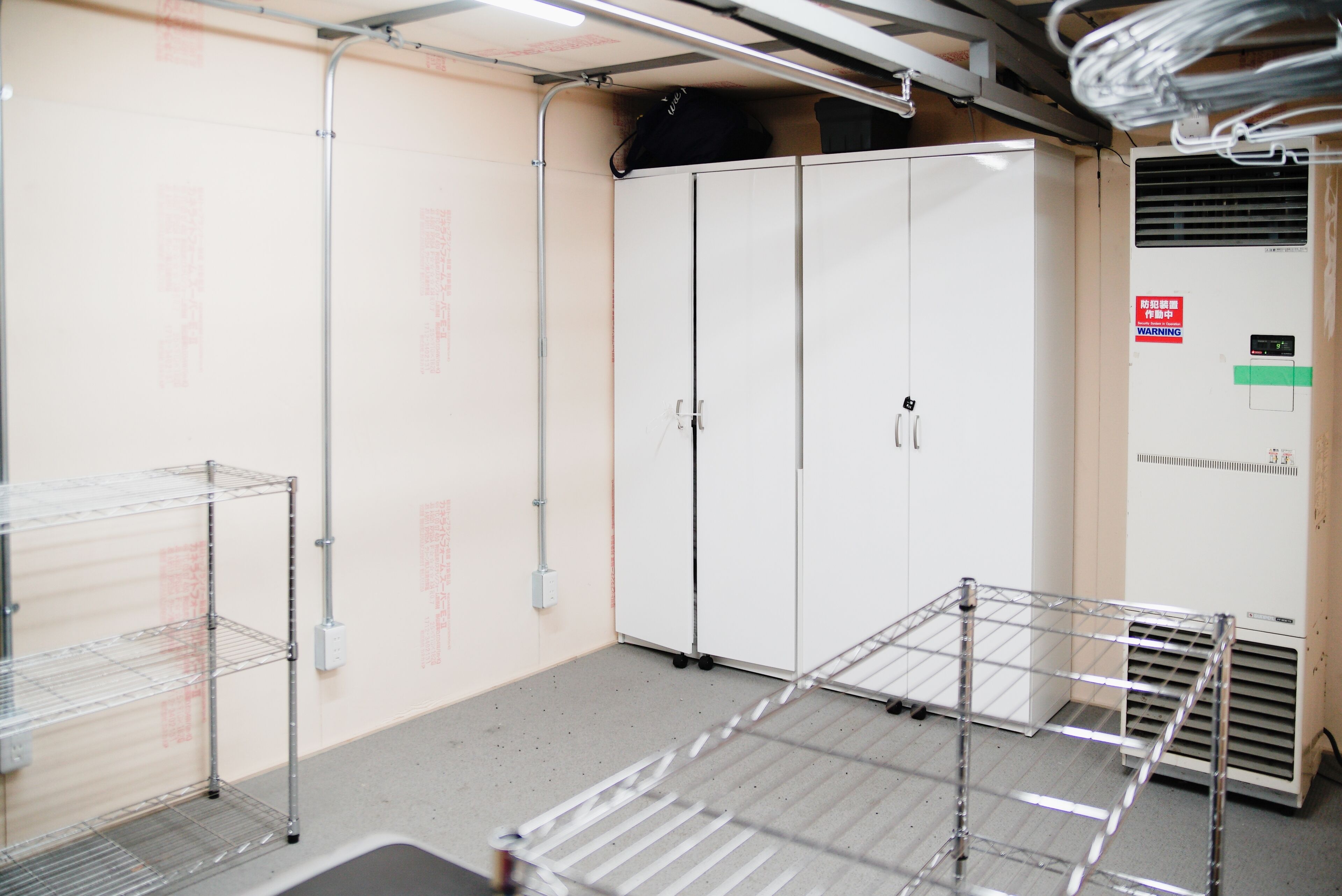 A room with metal shelving units, a white wardrobe, and a warning sign on the wall.