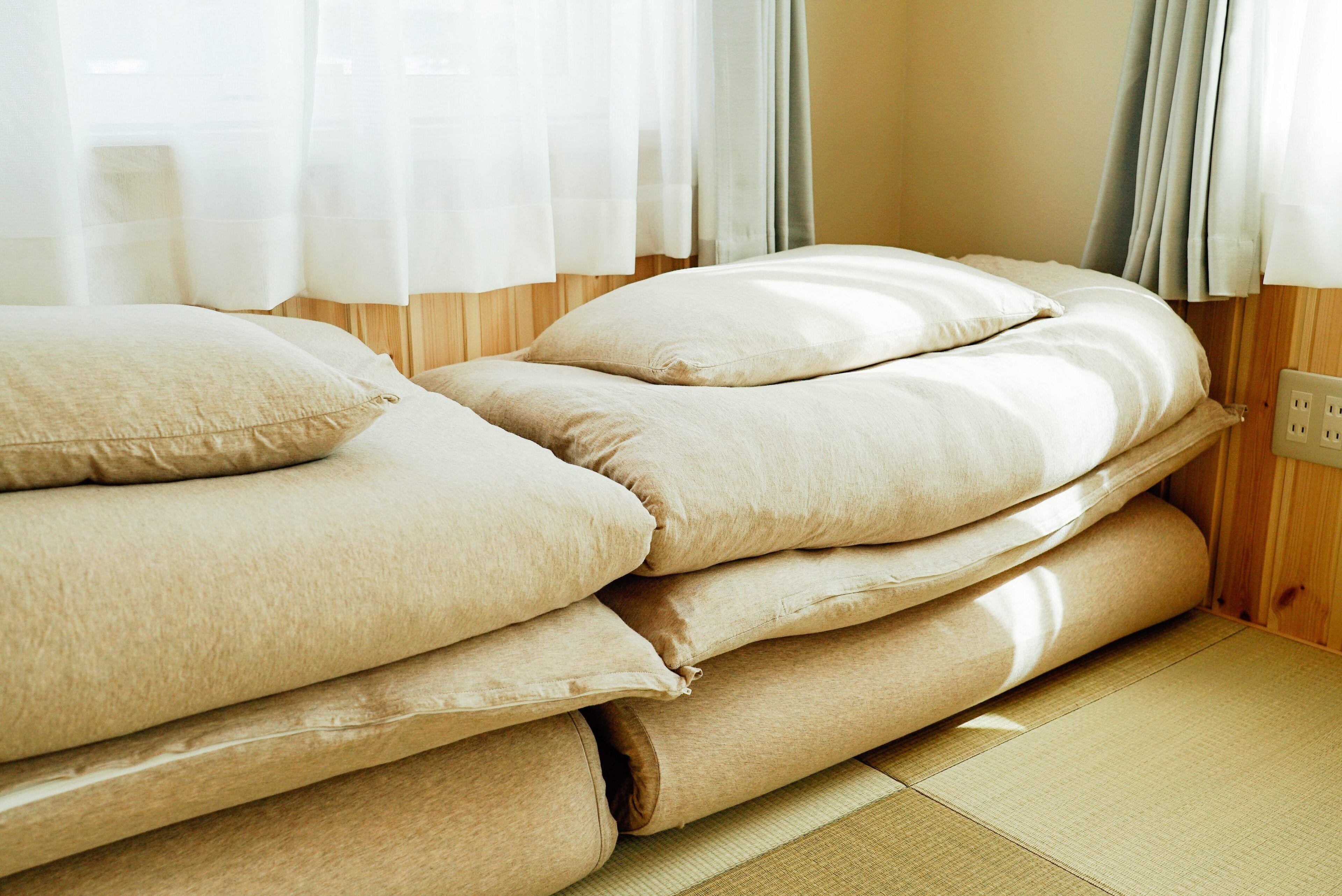 Een traditionele Japanse kamer met tatami vloeren, een laag bed met meerdere kussens en een houten wand.