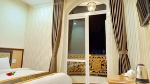 A hotel room with a bed, a bedside table with a teapot, curtains, and a decorative wall panel. - Sugar Land Villa Hotel Dalat (Xuan Huong - Da Lat)