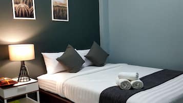 A neatly made bed with white linens and dark pillows, a bedside lamp, and two framed pictures on the wall.