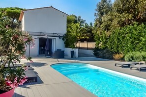 A swimming pool with a patio area, a covered outdoor seating area, and a building with a white facade.