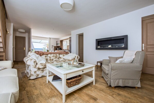 A living room with a sofa, a chair, a coffee table, and a kitchen area in the background.