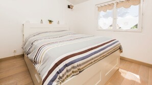 A bedroom with a bed, a window with curtains, a wall-mounted lamp, and a small plant on the nightstand. - Esprit du Sud Esterel (Sainte-Maxime)